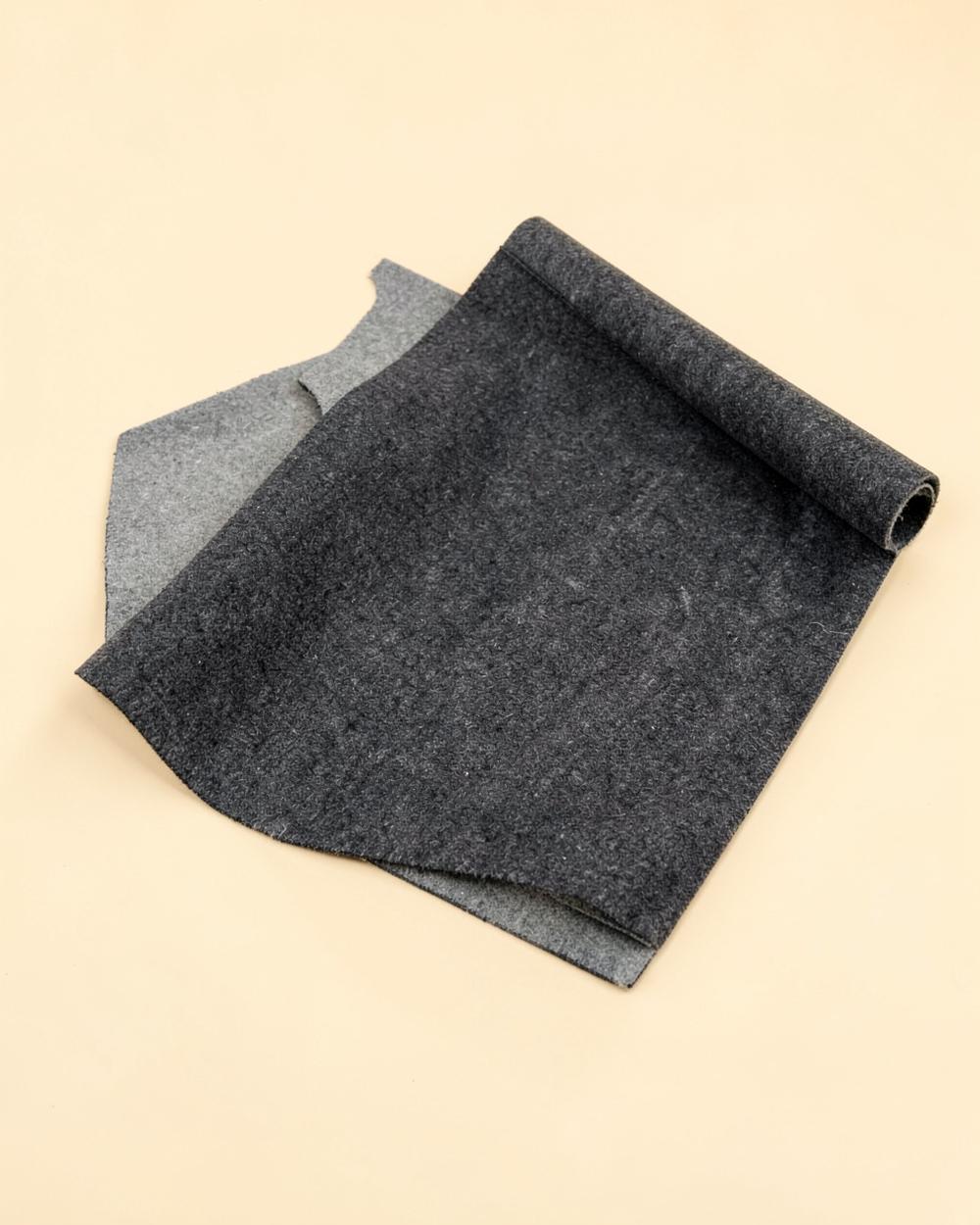Tapis de bureau gris anthracite légèrement enroulé sur un fond beige clair