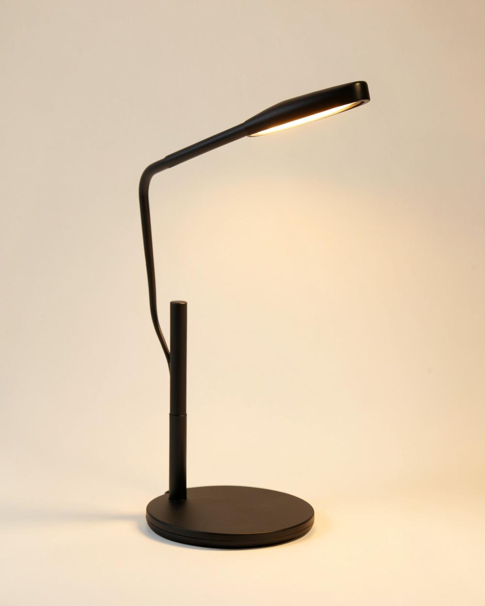 Lampe de bureau noire minimaliste allumée sur un fond beige clair