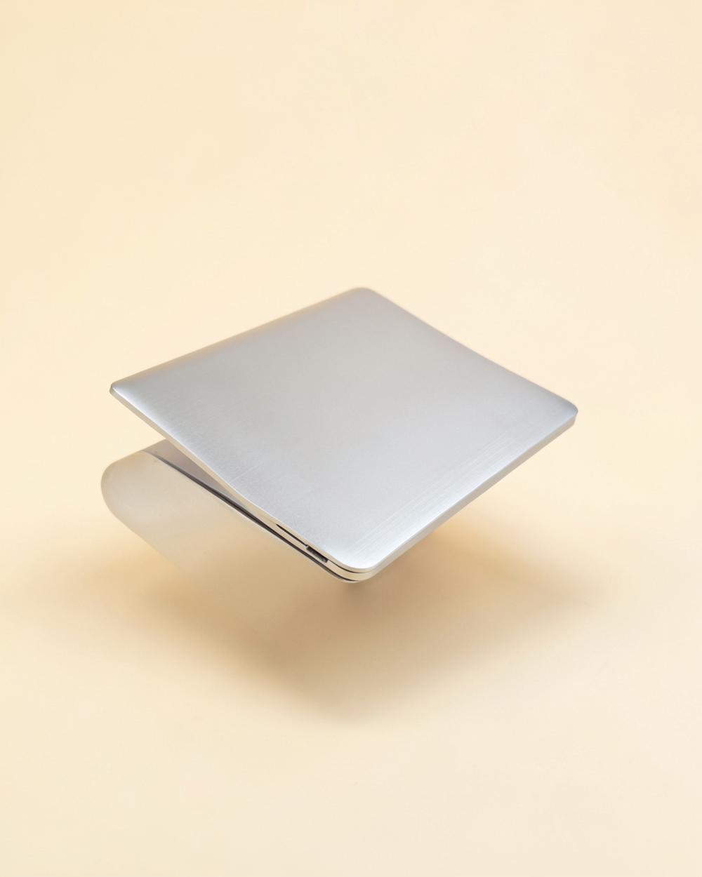 Support laptop en aluminium brossé présenté sur un fond beige clair
