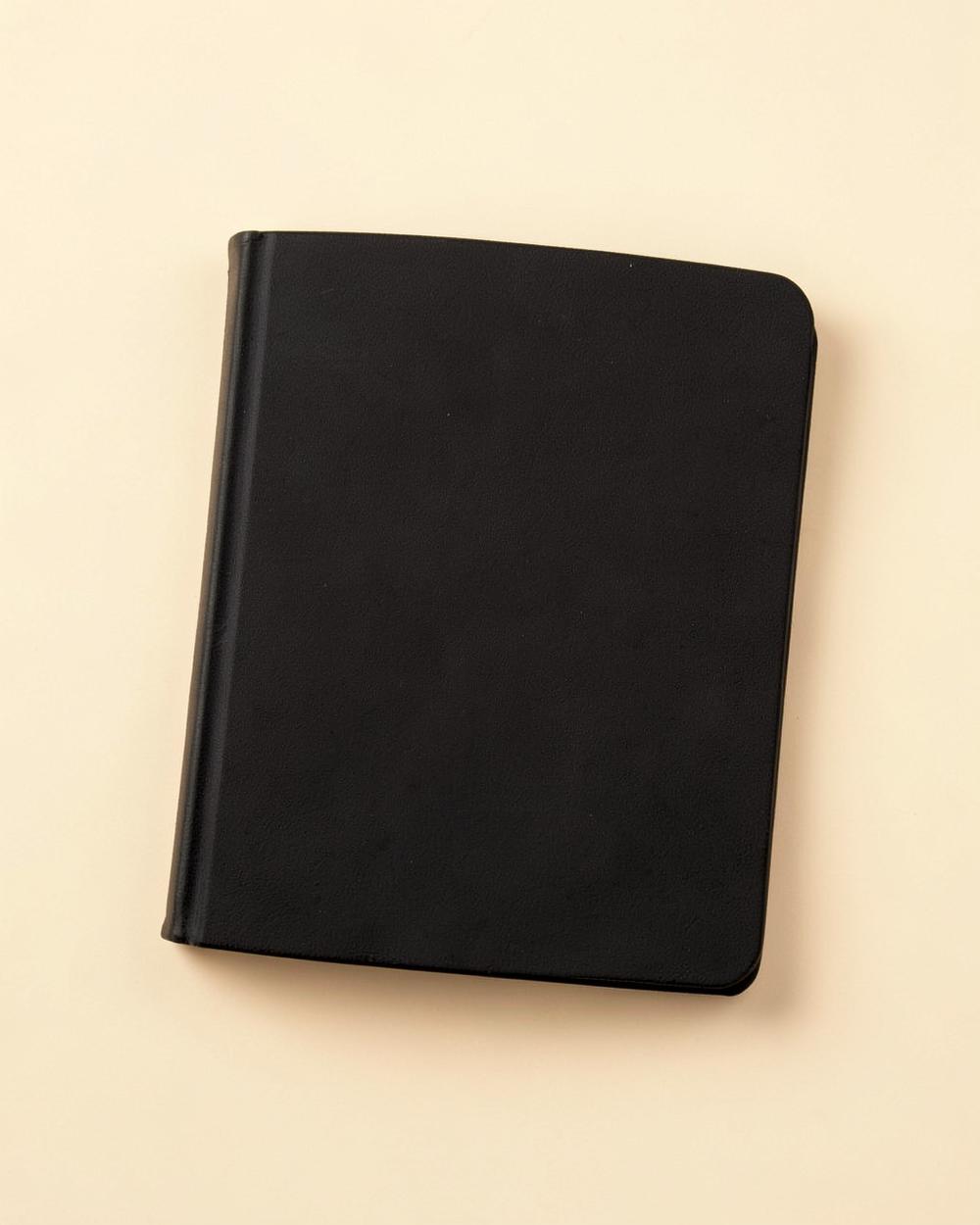 Carnet professionnel à couverture rigide noire posé sur un fond beige clair