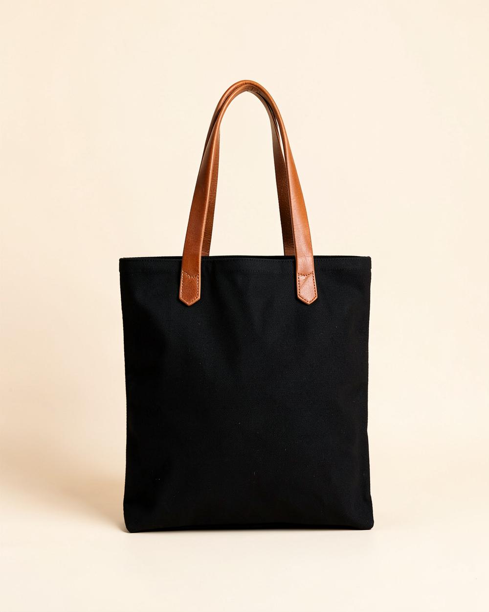 Sac de travail en toile noire avec anses en cuir brun sur un fond beige clair